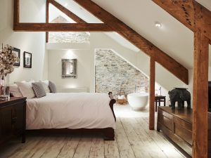 A free standing bath, roll top bed and exposed beams in this large and attractive bedroom at Devon Farmhouse